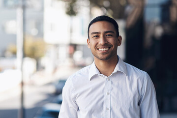 Smiling young man in a white collared shirt standing outdoors in a city setting.